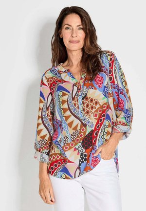 Blouse multicolore à motifs en tissu léger, avec un col en V et des manches trois-quarts. Présente des motifs géométriques en rouge, bleu et marron.