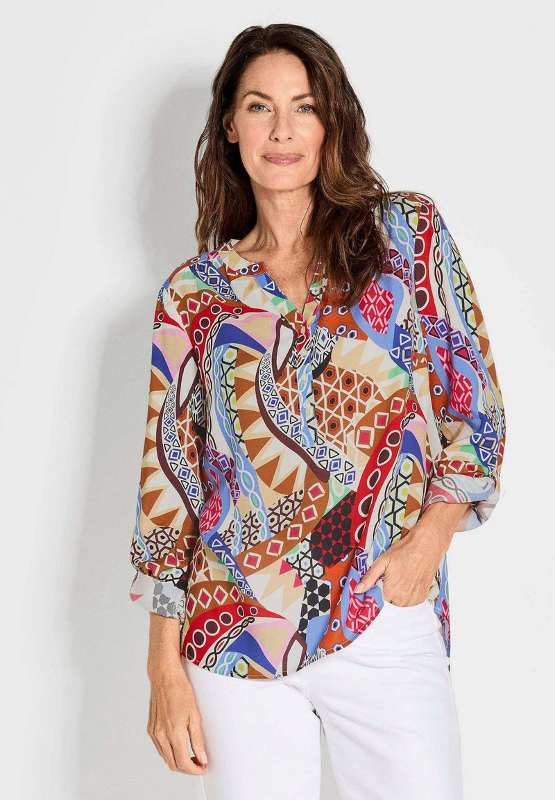 Multikleurige, patroonblouse van lichtgewicht stof met een V-hals en driekwartmouwen. De blouse heeft geometrische ontwerpen in rood, blauw en bruin.