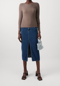 Maglione marrone a coste con maniche lunghe abbinato a una gonna midi in denim blu con uno spacco frontale. Sandali neri con tacco a blocco e una piccola borsa blu.