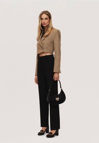 Blazer cropped a quadri marroni, pantaloni neri a vita alta, borsa nera con hardware dorato e scarpe nere con tacco a blocco decorate con un accento floreale.