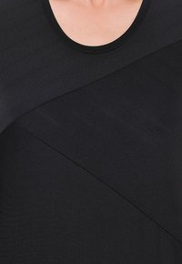 Černý top s kulatým výstřihem, strukturovanou tkaninou a asymetrickým designem s diagonálními liniemi, které vytvářejí vizuální zajímavost.