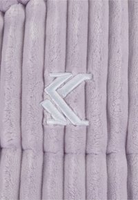 Lilla fleece-stoff med vertikal ribbestruktur, som har en hvit brodert logo. Myk tekstur med en fremtredende pelslignende utseende.