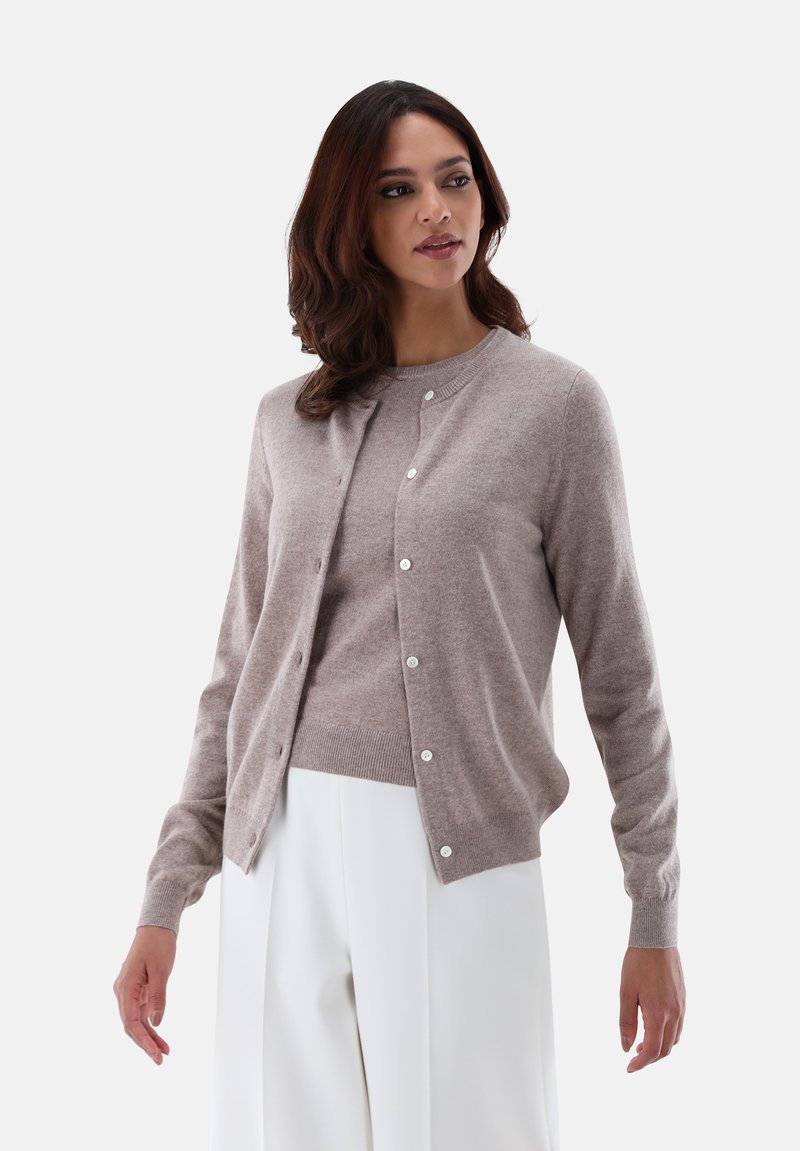 Light beige cashmere cardigan with a round neckline, seven buttons, ribbed cuffs, and hem, paired with a matching sweater and white trousers.