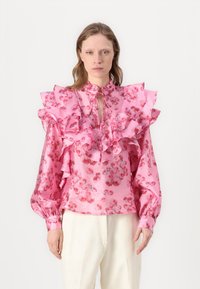 Blusa floreale rosa con generosi dettagli a ruota lungo il collo e le maniche, realizzata in tessuto morbido, con un nodo al collo.