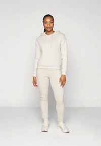 Sweat à capuche beige avec cordons, pantalon slim beige assorti et baskets claires. Texture lisse, design décontracté, style minimaliste.