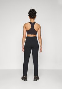Svart atletisk crop-top med racerback-design, parret med mørkegrå smale bukser lavet af blødt, strækbart stof, der har en elastisk talje.