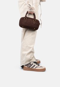Sac à main en daim marron avec des poignées courtes, associé à un pantalon large beige et des baskets beiges avec un imprimé léopard et des accents noirs.