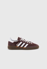 Sneaker in camoscio marrone con dettagli in pelle bianca, caratterizzata da tre strisce bianche, punta rotonda, lacci bianchi e suola in gomma marrone.