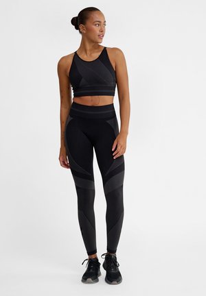 Sort atletisk crop top og leggings med teksturerede mønstre, sømløs design og tætsiddende silhuet. Parret med sorte sneakers.