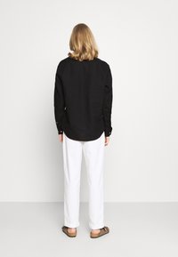 Černá košile s dlouhým rukávem a manžetami na knoflíky, kombinovaná s bílými kalhotami rovného střihu a hnědými sandály na neopren; hladký materiál a uvolněný střih.