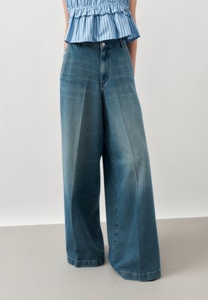 Person iført højttaljede, vidde blå denimjeans og en blåstribet top med flæsedetalje i taljen.