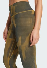 Tight-fitting leggings in dark gray with yellow abstract patterns, featuring a high waistband and textured fabric for structured support.