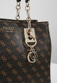 Brun og sort mønstret håndtaske med en guldfarvet lås, kædedetaljer og et 'G' logo charm. Fremstillet af syntetisk materiale.