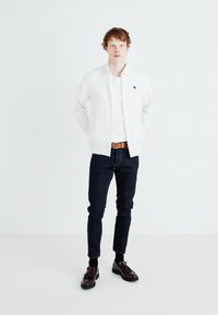 Bílé button-up košile přes bílé tričko, tmavé džíny, hnědý kožený opasek a tmavě burgundské boty; hladká tkanina, přizpůsobený střih.