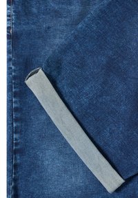 Tissu en denim bleu foncé avec un revers plié montrant le côté intérieur plus clair du matériau.