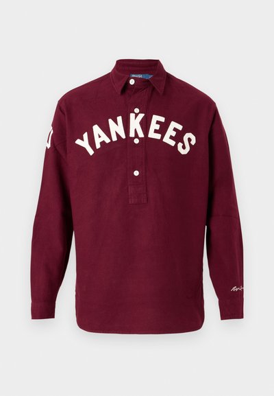 Burgundska košulja dugih rukava s ovratnikom na dugme, s natpisom "YANKEES" u bijelom izvezenom tekstu na prednjem dijelu i detaljem logotipa na rukavu.