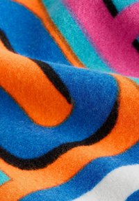 Värikäs fleece-peitto, jossa on aaltoilevat kuviot sinisen, oranssin, vaaleanpunaisen ja turkoosin sävyissä, mustilla ääriviivoilla. Pehmeä rakenne ja eläväinen muotoilu.