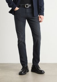 Tumedat teksased, slim fit-iga, koos musta nahkvöö ja poleeritud mustade kingadega. Riietust täiendab tumesinine nööbiga särk.