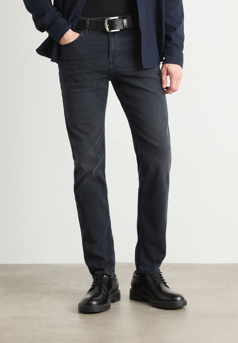 Tumedat teksased, slim fit-iga, koos musta nahkvöö ja poleeritud mustade kingadega. Riietust täiendab tumesinine nööbiga särk.