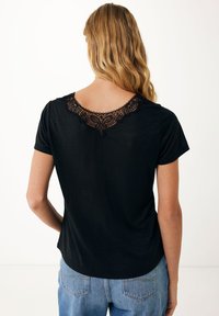 Top nero a maniche corte con un bordo decorativo in pizzo nero lungo il collo e una vestibilità casual, abbinato a jeans in denim azzurri.