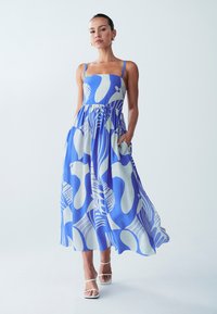 Maxi mekko sinivalkoisilla kuvioilla, jossa on istuva yläosa, olkaimet ja taskut, valmistettu kevyestä kankaasta, jossa on valuva hame.