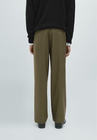 Wide-leg, olive green trousers with a smooth texture, featuring back pockets and tailored fit, paired with black shoes and a dark sweater.