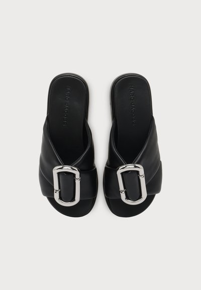 Paire de sandales slide noires avec de larges brides rembourrées et de grandes boucles ovales argentées, vues de dessus sur un fond neutre.