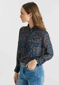 Long-sleeve, button-up blouse in dark blue with a leopard print pattern in brown and orange tones. Features two chest pockets and a sleek collar.