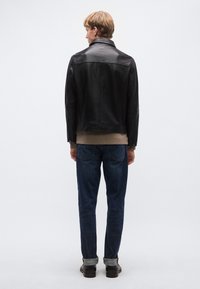 Fekete bőrdzseki klasszikus kialakítással, cipzáras záródással és sima textúrával, sötétkék farmerrel és barna cipővel párosítva.