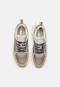 Sneaker beige con tomaia in mesh e suede, lacci blu navy e suola in gomma bianca. Presenta una linguetta sul tallone e dettagli del logo sulla linguetta.