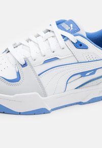 Baskets Puma blanches et bleues avec des lacets blancs, une semelle texturée et le logo Puma sur le côté et la languette, vues de profil.