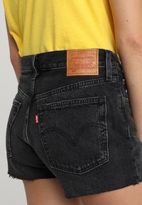 Black denim shorts with frayed edges, featuring a tan leather patch labeled "Levi Strauss & Co." and a small red logo on the side.