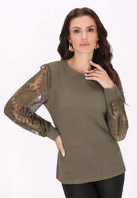 Pulover verde măsliniu cu un corp texturat, mâneci din dantelă semi-transparentă cu modele florale și manșete plisate. Finisaj neted pe corp.