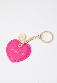 Heart-shaped pink keychain made of textured material, featuring embossed "ANNA FIELD" logo and a gold chain with round tag and keyring.
