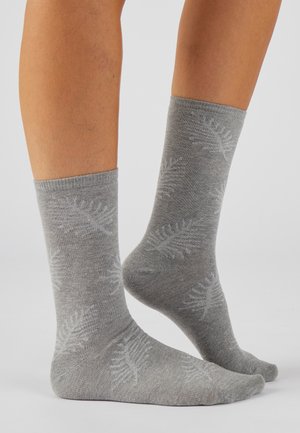 Benedenbenen met lichte grijze sneakersokken met subtiele varensbladpatronen op een effen lichte achtergrond.