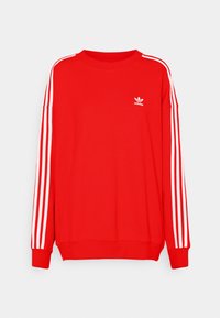 Sweatshirt Adidas rouge avec trois bandes blanches sur les manches et petit logo Adidas sur la poitrine gauche, présenté sur fond blanc.