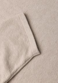 Tissu beige doux avec un coin plié montrant la texture et les détails de couture.