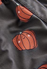 Tissu avec un fond sombre présentant des motifs répétés de citrouilles orange souriantes, aux contours bien définis et aux tiges vertes.