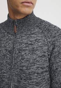 Maglione grigio con zip e colletto alto, caratterizzato da un motivo a maglia testurizzato e un piccolo tirazip marrone etichettato "BLEND."