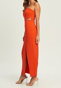 Trägerloses orange Maxi-Kleid mit seitlichem Cutout, das einen geschlitzten Rock und einen dünnen metallischen Akzent aufweist. Glattes, eng anliegendes Material.