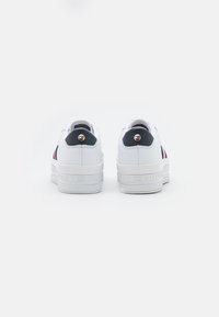 Weiße Plattform-Sneaker mit strukturiertem Sohle, featuring schwarze und rote Akzente sowie ein Logodetail auf der Rückseite. Glattes synthetisches Material.