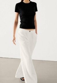 Top corto nero a maniche corte abbinato a pantaloni bianchi larghi, con dettagli di bottoni frontali e una silhouette rilassata.