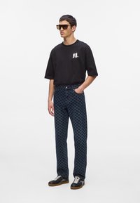 Must have lühikeste varrukatega must t-särk logoga, millele on sobitatud tumedast sinisest houndstooth-mustriga teksad ja mustad jooksujalatsid valgete paeltega. Prantsuse päikeseprillid.