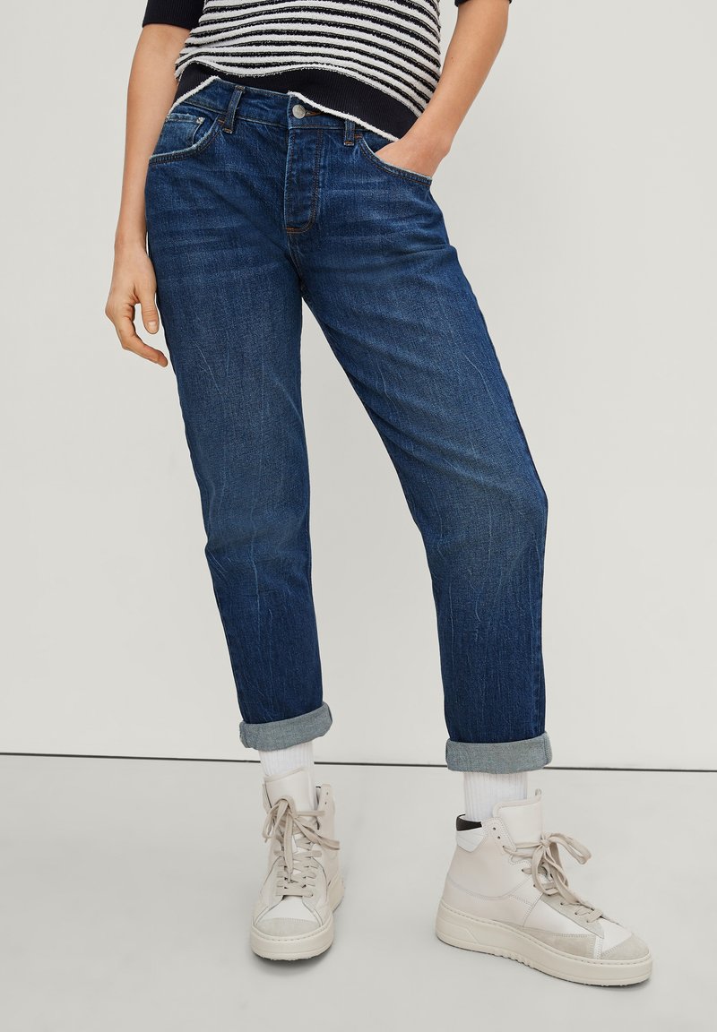 Jeans in denim di un blu scuro, con una vestibilità comoda e orli arrotolati. Abbinati a sneakers alte bianche e un maglione a righe.