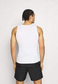 Weißes ärmelloses Tanktop aus atmungsaktivem Material, eng anliegendes Design, glatte Textur, mit klassischem Rundhalsausschnitt. Getragen mit schwarzen Shorts.