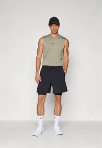 Moška športna oprava s prilagojeno olivno zeleno majico brez rokavov in mornarsko modrimi hlačami z nastavljivim vrvico. Izgled dopolnjujejo beli supergi in nogavice.