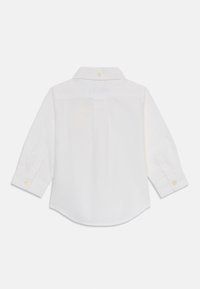 White, long-sleeve button-up shirt with a collar, featuring a back pleat, rounded hem, and single-button cuffs. Fabric appears smooth.