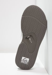 Semelle en caoutchouc gris avec un motif zigzag texturé ; comporte un logo "REEF" et un insert pour le confort du pied.