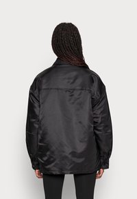 Black satin jacket with a loose fit, long sleeves, and a shirt collar. Features buttoned cuffs and a smooth, glossy texture.