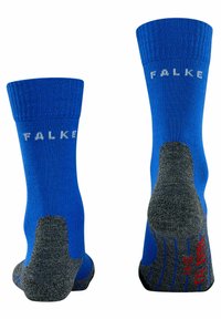 Calcetines azules con puños acanalados, con un talón y puntera gris reforzados, y el logo "FALKE" en blanco. La suela tiene detalles en rojo.